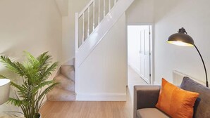 A staircase with white railings, a grey sofa with an orange pillow, and a floor lamp. - Host & Stay | Fountains Cottage (Guisborough)
