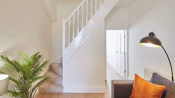 A staircase with white railings, a grey sofa with an orange pillow, and a floor lamp.