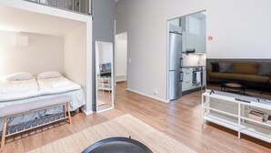 A modern apartment with a loft bedroom, a kitchenette, a living area with a sofa and a TV stand, and a dining area. - Renovated Loft in a Historical Downtown Building (Tampere)