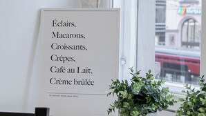 A framed menu listing Parisian dishes on a white wall near a window with a city view. - Renovated Loft in a Historical Downtown Building (Tampere)