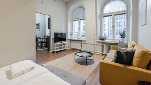 A modern living room with a sofa, a TV, and a dining area with a table and chairs. - Renovated Loft in a Historical Downtown Building (Tampere)
