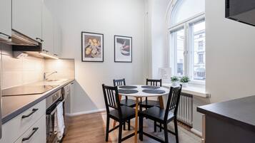 A modern kitchen with a dining area, featuring a round table with chairs, a built-in oven, and a window with a view of the street.