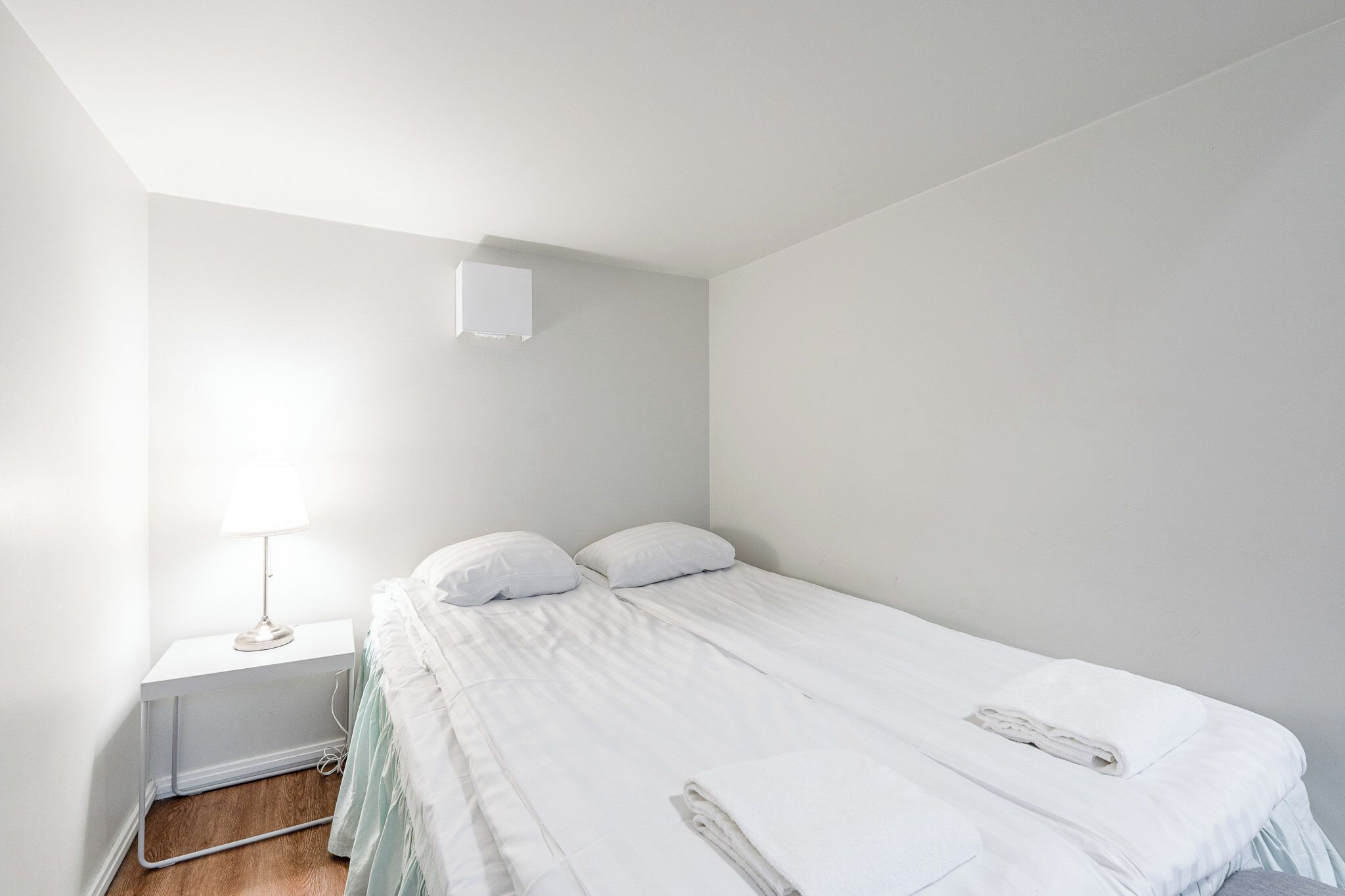 A simple, clean room with a bed, a nightstand, and a lamp.