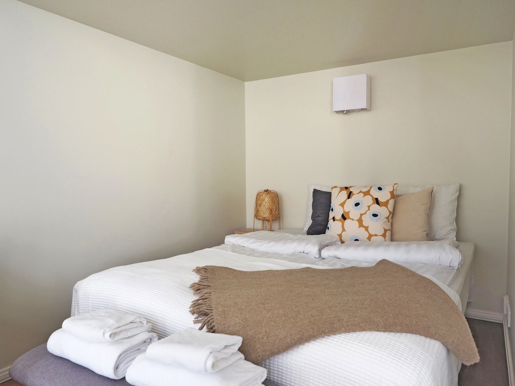 A neatly made bed with white and beige bedding, a brown throw blanket, and a small bedside table with a woven basket.