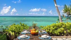 A table set for dining with a view of the ocean and palm trees.