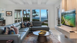 A modern living room with a large sectional sofa, a round coffee table, and a large flat-screen TV mounted on the wall.