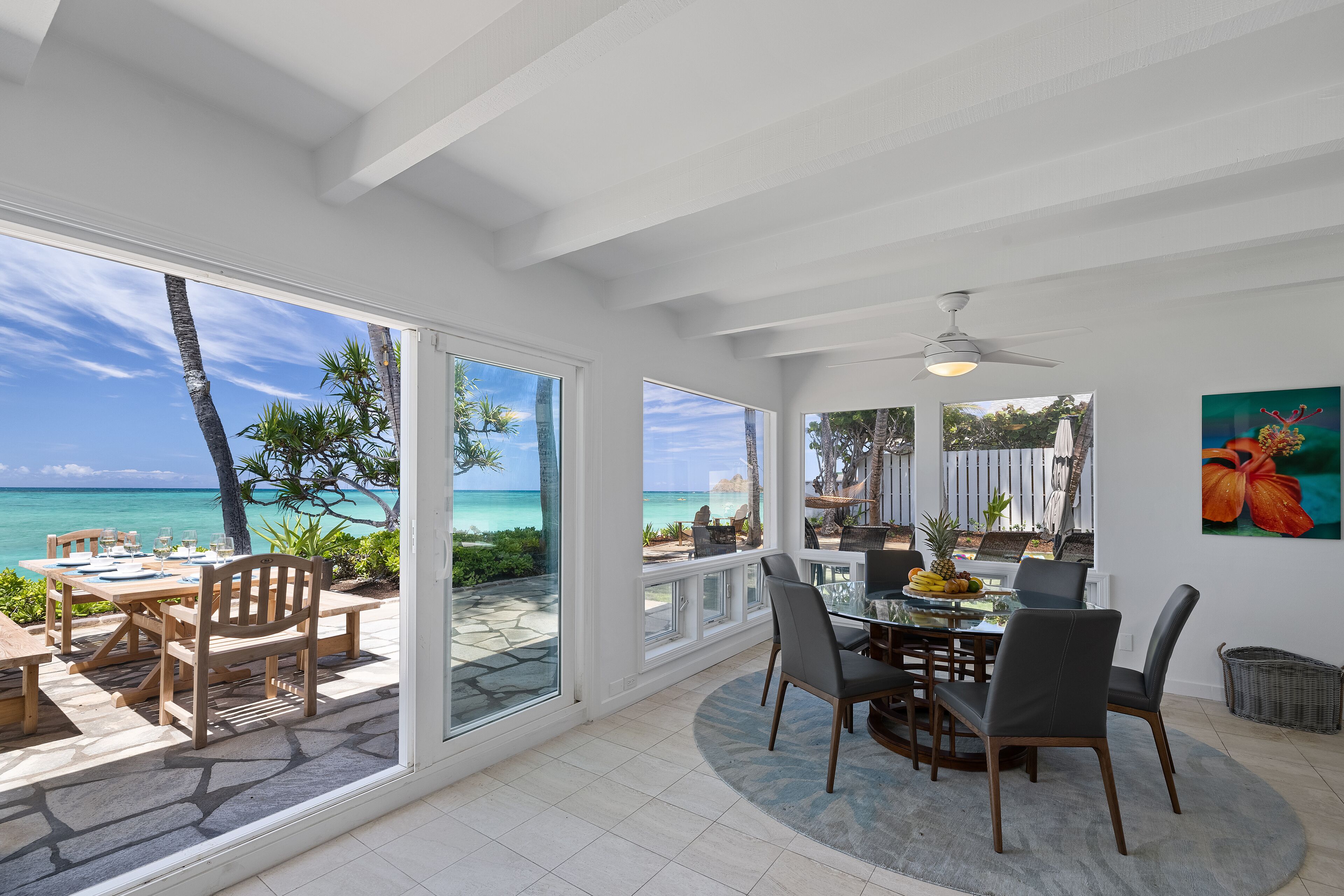 A spacious dining area with a view of the ocean, large windows, and a ceiling fan.