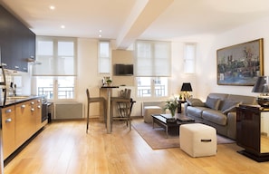 Um apartamento moderno com cozinha, sala de jantar e sala de estar. Apresenta piso de madeira, um sofá, uma mesa de centro e uma pintura na parede.