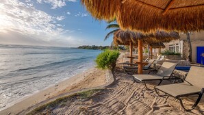 A beachside resort with thatched umbrellas, lounge chairs, and a view of the sea. - Beautiful condo with ocean views, AC and pool! (Akumal)