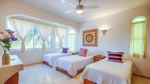 A room with two single beds, a ceiling fan, a wall-mounted light fixture, and a window with curtains. - Beautiful condo with ocean views, AC and pool! (Akumal)