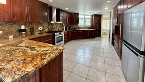 A modern kitchen with dark wood cabinets, granite countertops, stainless steel appliances, and recessed ceiling lighting. - Santorini In Puerto Rico Inc. Since 2017... (Río Grande)