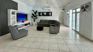 A modern living room with a sectional sofa, a flat-screen TV, and a potted plant. - Santorini In Puerto Rico Inc. Since 2017... (Río Grande)