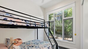 A bunk bed with a patterned bedspread, a window with a view of greenery, and a door with a yellow lock.