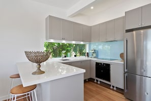A modern kitchen with grey cabinets, a stainless steel refrigerator, and a central island with stools.