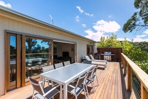A deck with a dining table and chairs, a grill, and a view of the surrounding landscape. - Strathlea (Lorne)