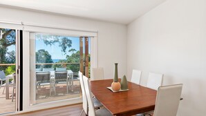 A dining area with a wooden table, white chairs, and a view through a glass door to an outdoor deck. - Strathlea (Lorne)