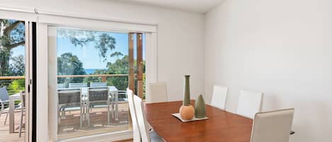 A dining area with a wooden table, white chairs, and a view through a glass door to an outdoor deck.