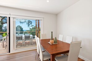 A dining area with a wooden table, white chairs, and a view through a glass door to an outdoor deck. - Strathlea (Lorne)
