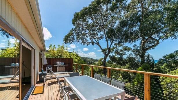 An outdoor deck with a dining table and chairs, a barbecue grill, and a view of the surrounding landscape. - Strathlea (Lorne)
