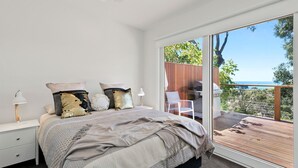 A bedroom with a large bed, two bedside tables, a nightstand, and a view of a deck and outdoor area. - Strathlea (Lorne)