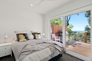 A bedroom with a large bed, two bedside tables, a nightstand, and a view of a deck and outdoor area. - Strathlea (Lorne)