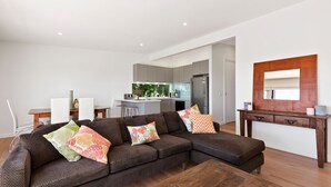 A modern living room with a sectional sofa, a wooden coffee table, and a kitchen in the background. - Strathlea (Lorne)