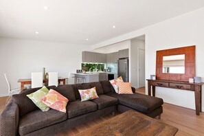 A modern living room with a sectional sofa, a wooden coffee table, and a kitchen in the background. - Strathlea (Lorne)
