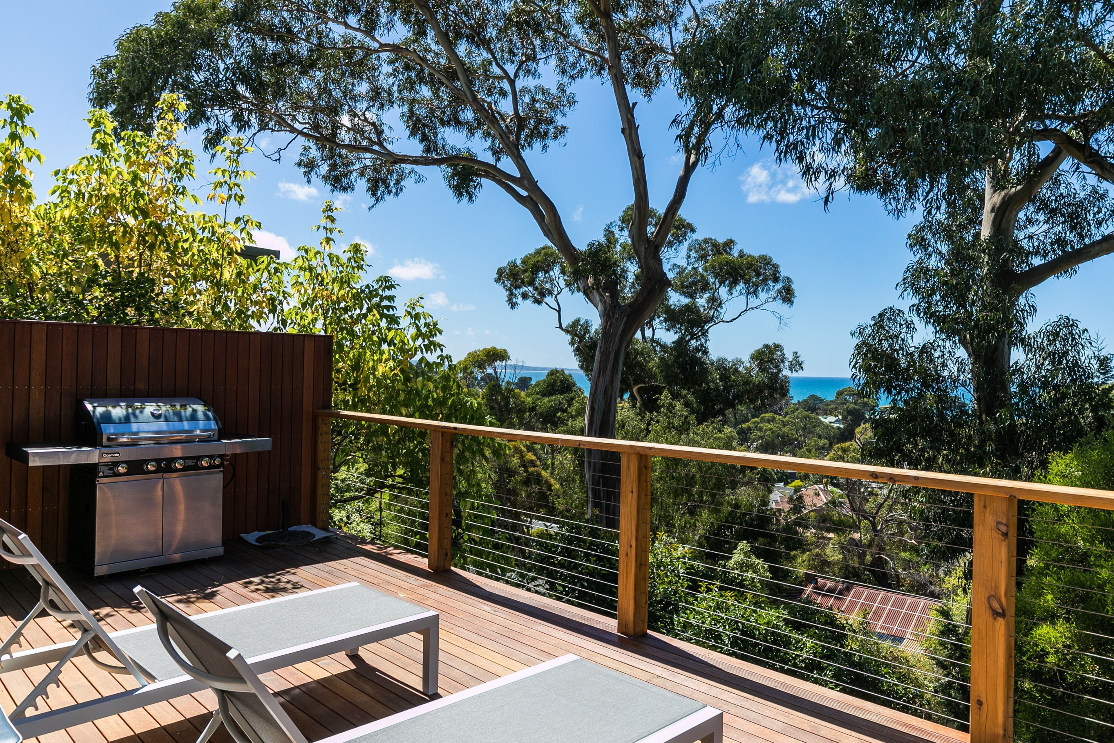 A deck with a barbecue grill, lounge chairs, and a view of the sea.
