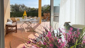 Une terrasse avec une table et des chaises, un parasol jaune et un pot de fleurs orné de fleurs roses.