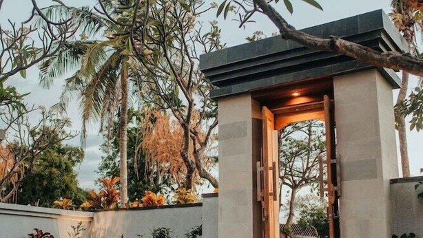 A modern entrance with a glass door, surrounded by lush greenery and palm trees. - New Sunari Lovina Beach Resort (Buleleng)