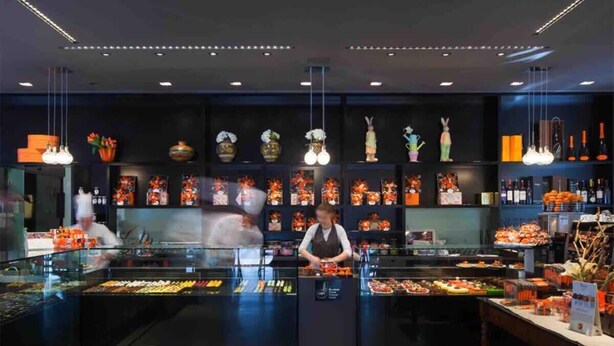 Een modern restaurantinterieur met een centrale balie, decoratieve muurkunst en hangende verlichting.