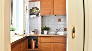 Een kleine keuken met houten kastjes, een spoelbak en een raam met gordijnen.