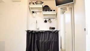 Una cucina funzionale con pareti bianche, una tenda nera e scaffali pieni di utensili da cucina.