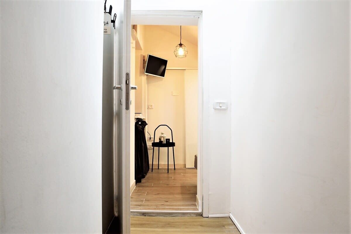 Un couloir étroit avec un plancher en bois, une chaise noire et un téléviseur fixé au mur.