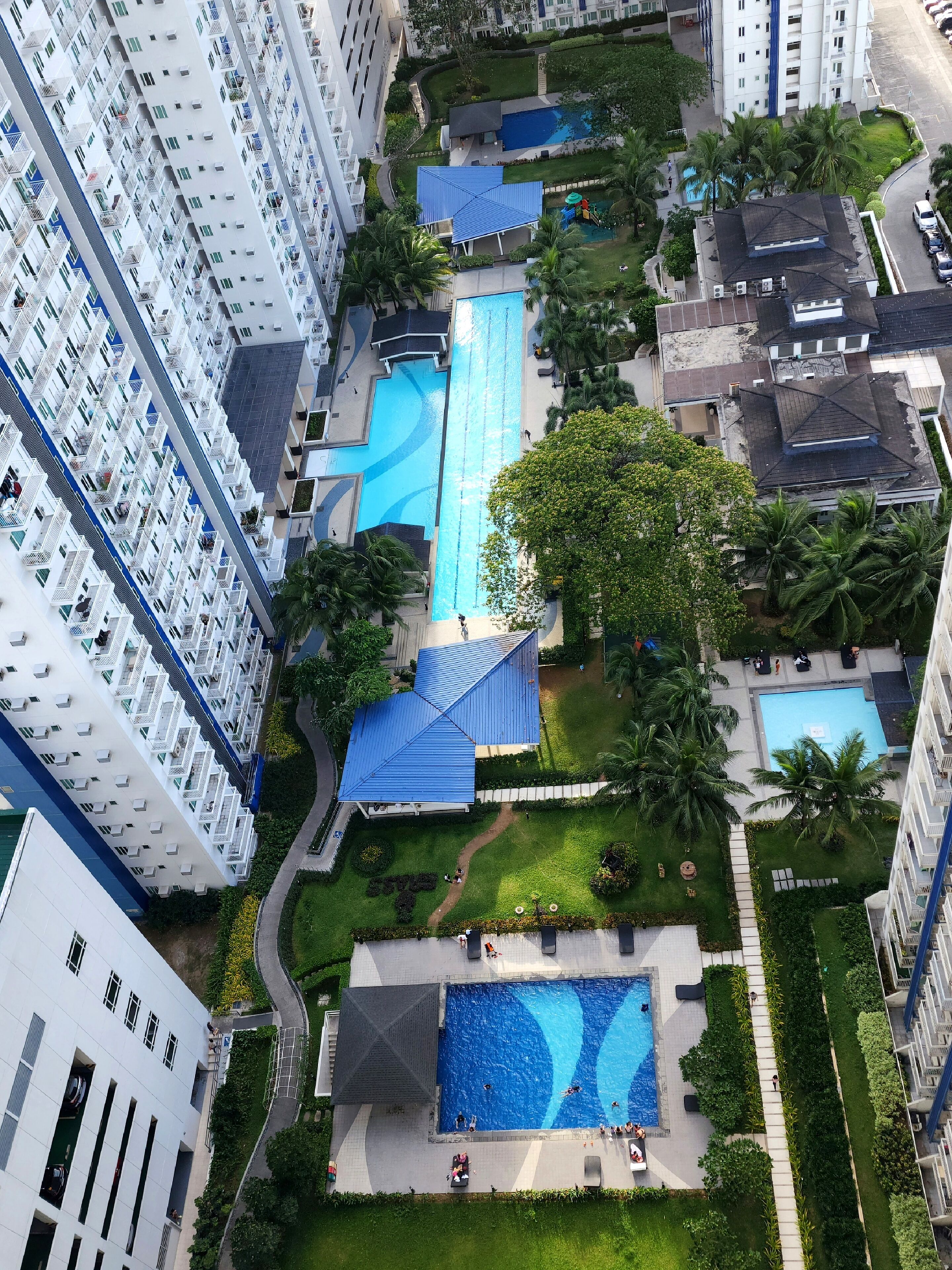 Un edificio residencial de altura con varios balcones, una piscina central y áreas verdes circundantes.