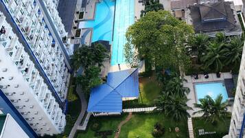 Un edificio residencial de altura con varios balcones, una piscina central y áreas verdes circundantes.