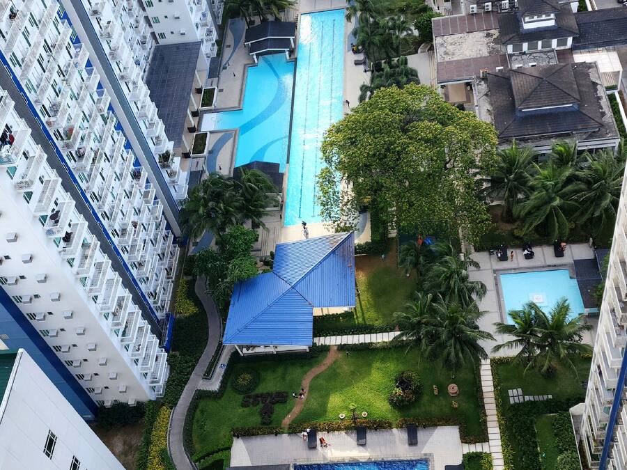 Un edificio residencial de altura con varios balcones, una piscina central y áreas verdes circundantes.
