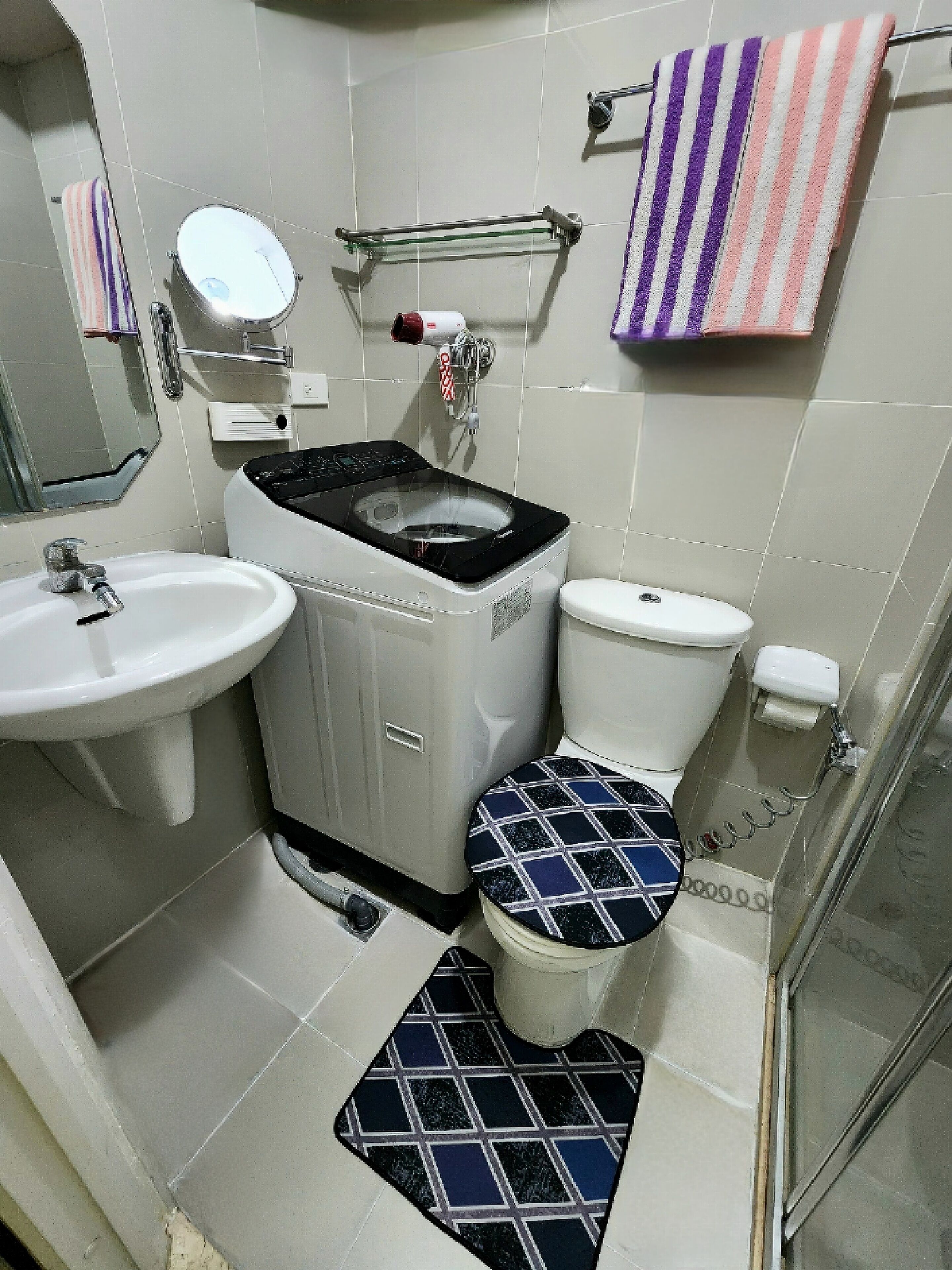 A bathroom with a sink, toilet, and bidet. There is a towel rack with striped towels and a glass shower enclosure.