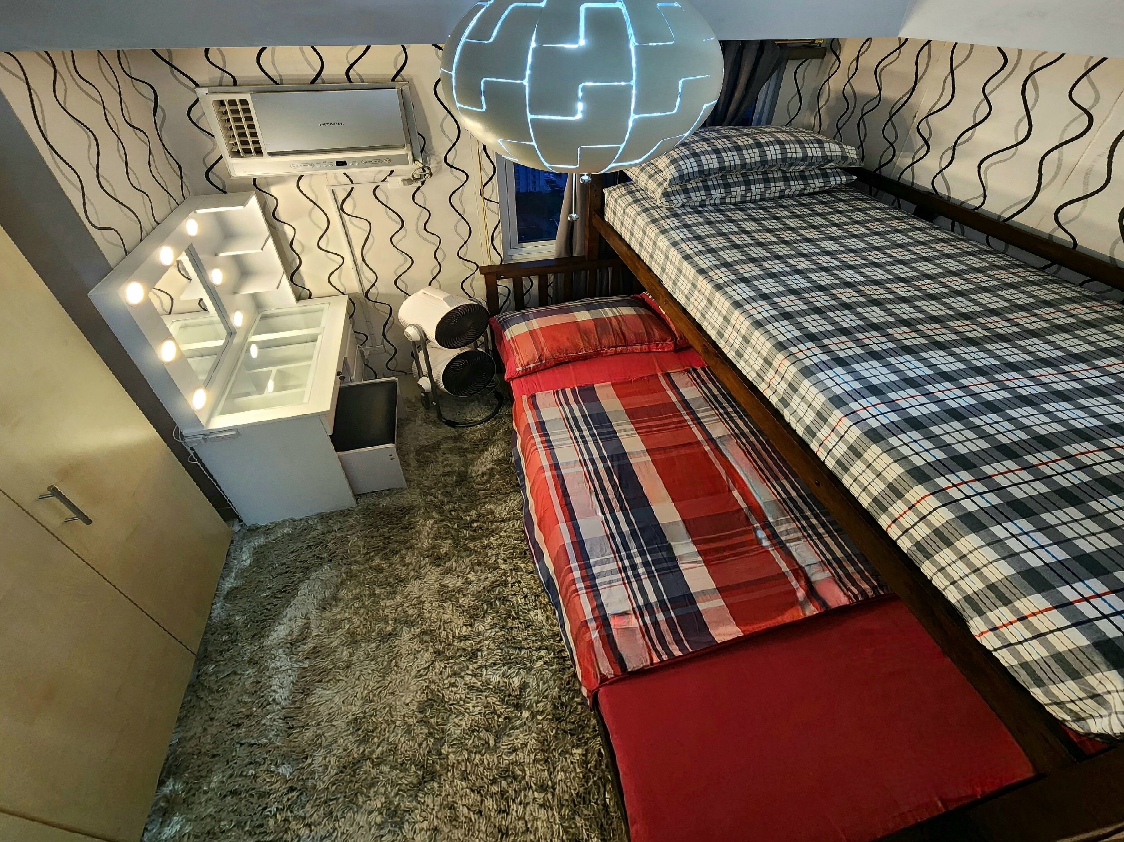 A compact bedroom with a bed, a vanity with lights, a heater, and a globe light fixture.