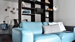 Uma sala de estar moderna com um sofá de couro azul, uma estante preta e branca e uma pequena mesa lateral com uma luminária.