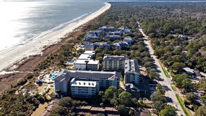 An aerial view of a coastal hotel with multiple buildings, a beach, and a forested area.