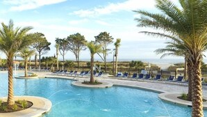 A pool with palm trees and lounge chairs, surrounded by a fence.
