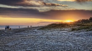 A beach with people walking, a sunset, and dunes.