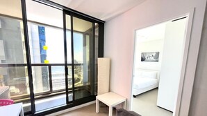 Une chambre moderne dotée d’une grande porte-fenêtre coulissante donnant sur un balcon, d’un lit blanc et d’une petite table blanche.