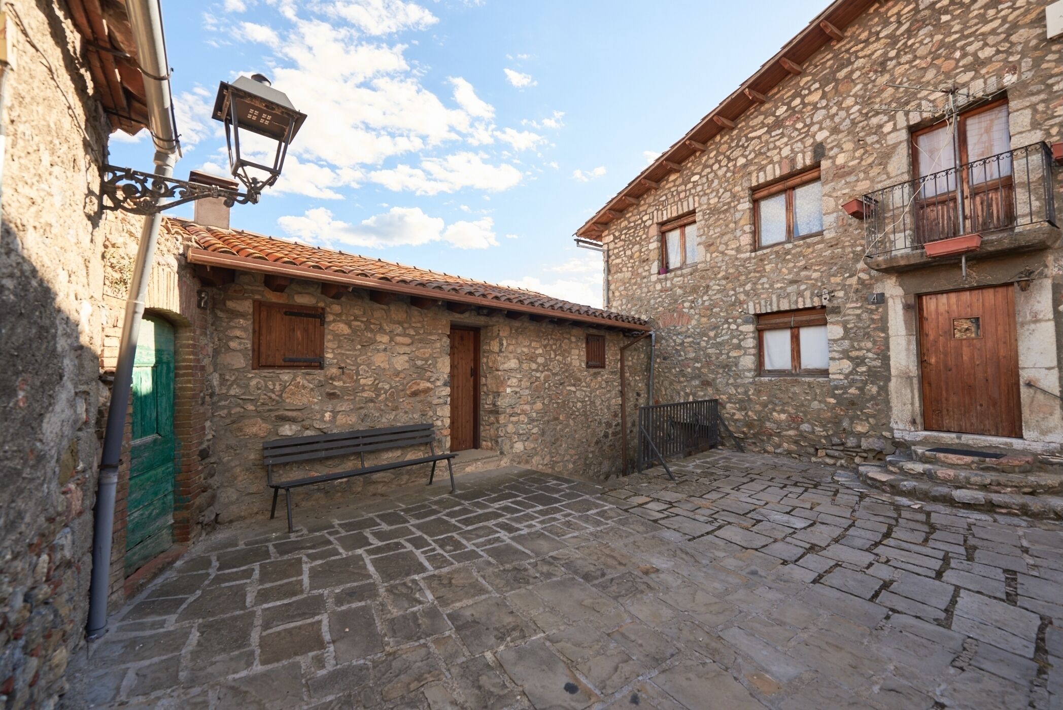 Un cortile in pietra con pavimentazione in ciottoli, edifici in pietra, porte in legno e una panchina.