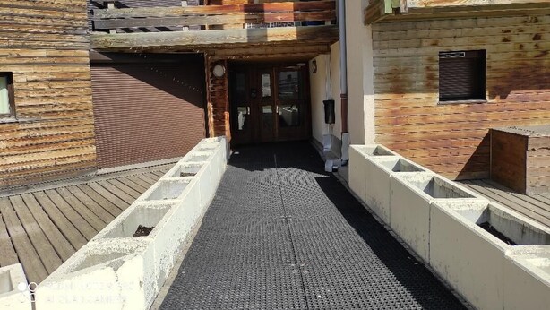 A narrow pathway leading to a wooden building with a balcony.