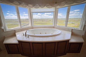 Ein Badezimmer mit einer freistehenden Badewanne, großen Fenstern und Blick auf eine sumpfige Landschaft.