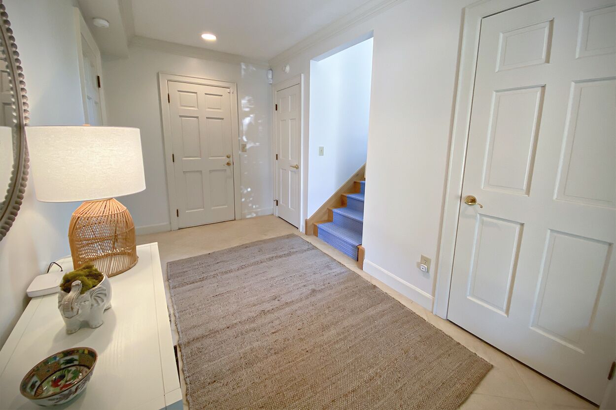 A hallway with a white door, a blue staircase, and a white console table with a lamp and decorative items.