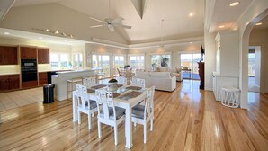 Amplia sala de estar con mesa de comedor, mobiliario blanco y vista al exterior.