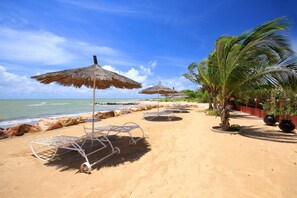Ein Strand mit Reetdachschirmen, Liegestühlen und Palmen.